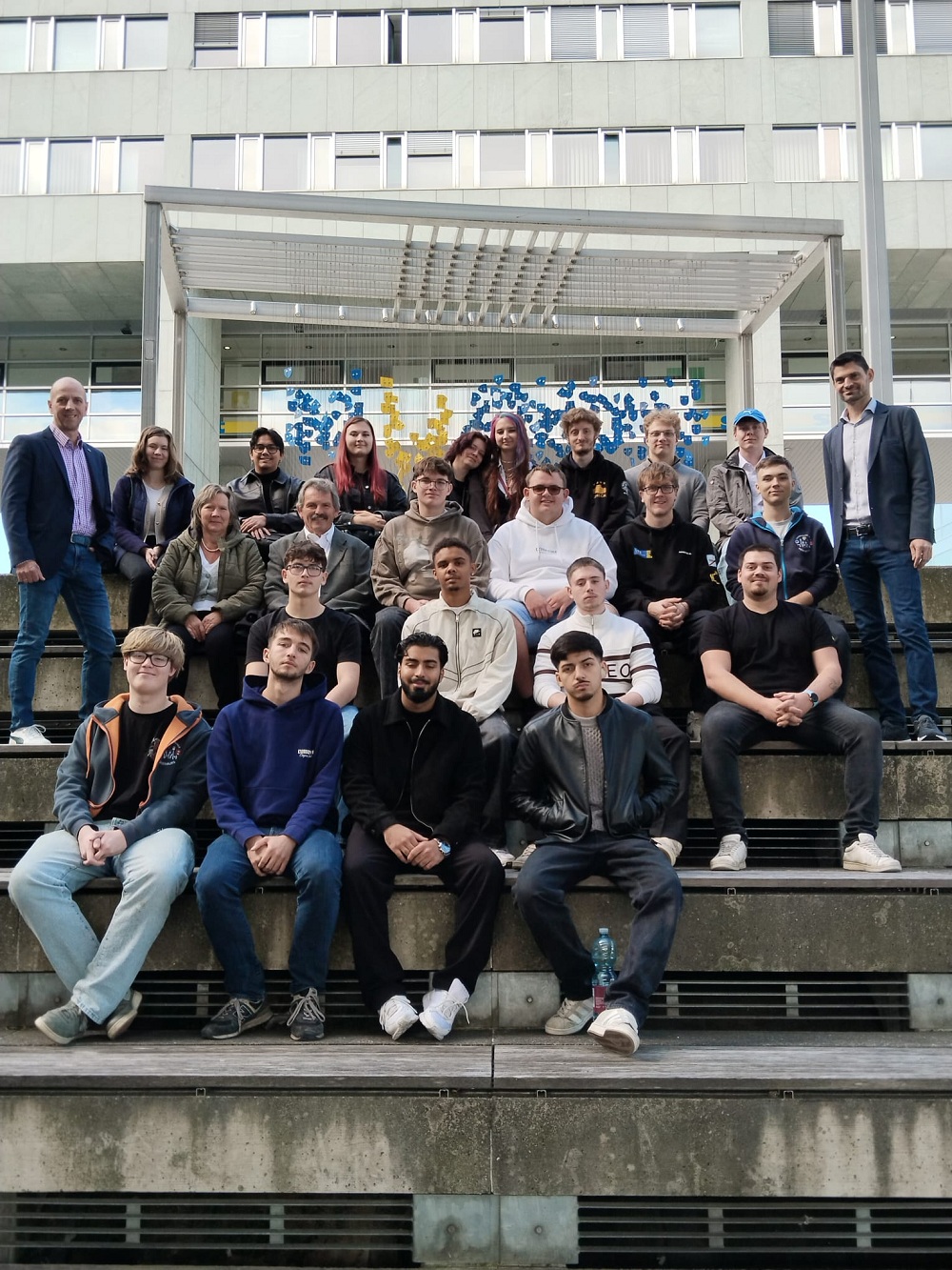 Gruppe von Personen sitzt auf Betontreppen vor modernem Gebäude in Wien